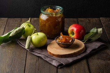 Tasty homemade apple jam, confiture in a glass jar with apples on a black wooden table