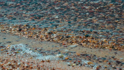 Close-up photo of stones on the shore of the blue sea with waves