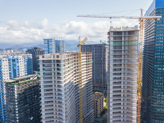 Fototapeta premium Drone view of the construction of multi-storey buildings on a summer day against the backdrop of mountains