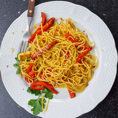 Up view. Close-up of rice noodle dish with curry, red bell peppers, parsley and tofu. Vegan food. No people.