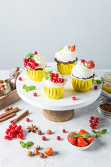 Delicious cupcakes with berries and white cream on a cake pan on a light background. Beautiful cakes with a place for text and for your design