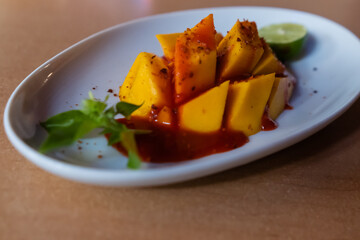 Plate of chopped mango with Mexican chamoy sauce and blurry background