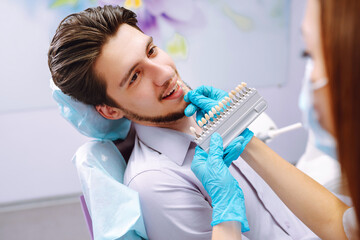 Young man at the dentist's chair during a dental procedure. Overview of dental caries prevention. Dentist examining patient's teeth in modern clinic. Healthy teeth and medicine concept.