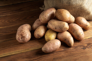 Big bunch of potatoes after harvest lying on vintage wooden boards with a potato sack in the background