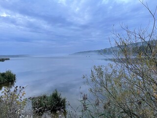 Evening view of the lake, where the fog spreads, fishermen catch in the distance on boats. The sky merges with the lake