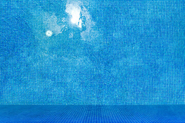 Top view of clear water in a blue tile swimming pool background.