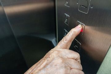 Close-up with selective focus of an elderly woman's finger squeezing a thumb inside the elevator.