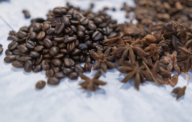 Small piles of coffee beans and star anise seeds on white surface