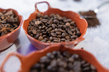 Three pots of roasted coffee beans and star anise seeds on white surface