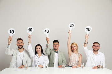 Panel of judges holding signs with highest score at table on beige background