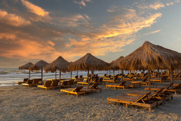 Wooden chairs with umbrellas on the sea shore in the beautiful light of the sunset. Beautiful colors of the sky