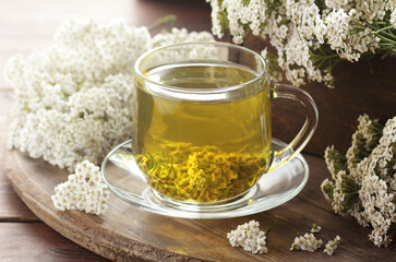 Yarrow herbal healing tea or decoction with fresh milfoil flowers close on rustic table on wooden...