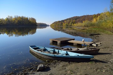 Naklejka na ściany i meble On the river bank near the pier there are two wooden boats against the background of the autumn forest 