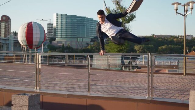 Businessman with a business briefcase in his hands overcomes an obstacle being late for an important meeting. Entrepreneur or office worker rushing to work. Man in formal wear is jumping parkour