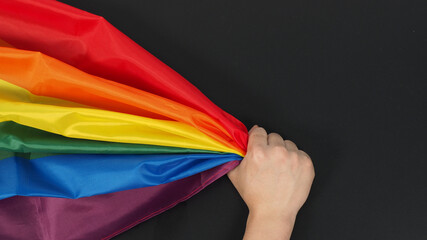 Hand is holding rainbow flag on black background.