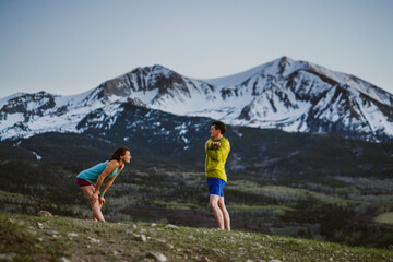 Two friends stretch together before trail running in the mountains