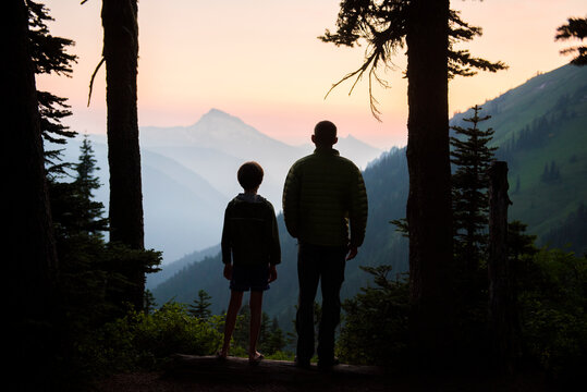 A boy and his dad enjoy the sunset together while camping.