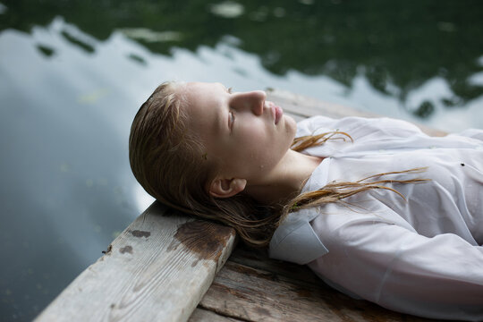 Blonde teenage girl  in white shirt with wet hair is lying by the lake