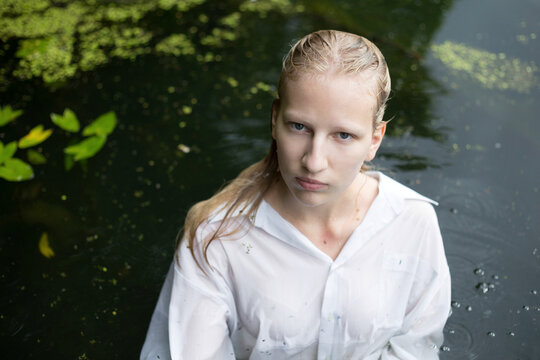 Blonde albino woman in white shirt with wet hair swim in local pond