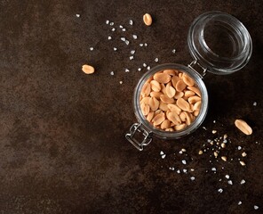 Glass jar of roasted salted peanuts on a dark background with space for text. Top view. Flat lay  