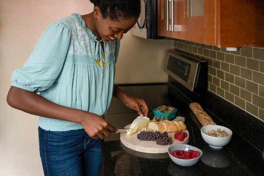 Woman cutting brie cheese on a charcuterie board in her home kitchen