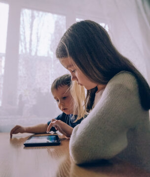 Little girl and boy playing on a gadget tablet pc at home at the table