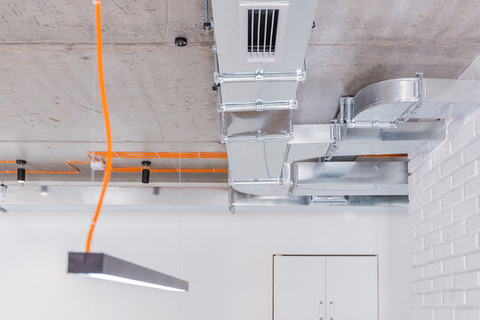 Concrete ceiling with orange electrical wiring and luminaires with ventilation ducts