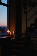 The child lights the menorah for Hanukkah on the windowsill. The boy in the kippah sitting by the window. Jewish holiday. Tradition is a religious ritual. Sunset. The first star. Judaism