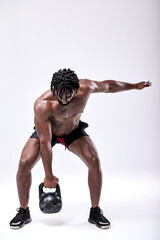 Young African man in shorts training exercises, Fit afro shirtless male doing kettlebell workout session, doing squats with weight. Fitness and bodybuilding lifestyle concept. Full-length portrait