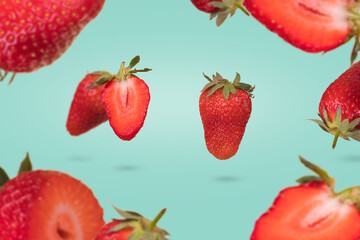 Creative composition with floating levitating ripe strawberries on a pastel turquoise background.