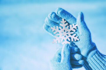 Female hands in a blue gloves with a snowflake on the snow background. Christmas concept.