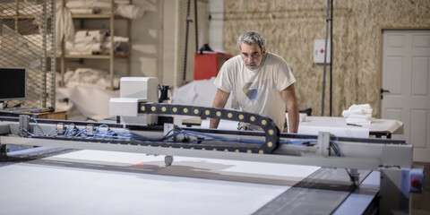 Fototapeta na wymiar Technician works on CNC digital cutter machine for cutting textile
