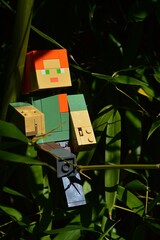 Obraz premium LEGO Minecraft large action figure of Alex sitting on side branch of real bamboo plant of Phyllostachys genus, in bamboo monoculture foliage, autumn daylight sunshine. 