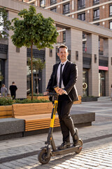 optimistic caucasian guy in formal suit riding scooter, along city street. Handsome businessman or office worker enjoy leisure time outdoors, have rest, using smart vehicle, electro scooter © Roman