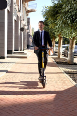 Handsome Caucasian Guy In Formal Suit Riding Smart Electro Scooter Going At Work, Holding Package With Food Breakfast Meal, In The Morning Or Launch. People Lifestyle, Modern Technologies Vehicle