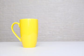 Big yellow ceramic mug, cup of american coffee on a white table against light brick wall with copy space
