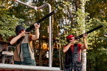 Young caucasian skilled people in goggles and headset on tactical gun training classes, aiming rifle at target. Shooting and Weapons. Outdoor Shooting Range At Summer Evening. focus on female