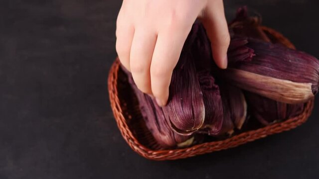 Hand putting in a basket som latin traditional food made of corn and wrapped in purple corn leaves on a black wooden table 