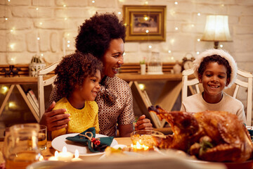 Cheerful black mother and her kids talk and have fun during Christmas lunch at dining table.