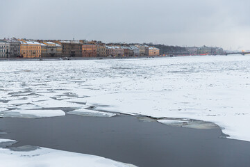 Winter view of the Neva River and the historical center of St. Petersburg. Historical buildings on the embankment. Cracked ice floes on the surface of the water. Cold winter weather. Travel to Russia.