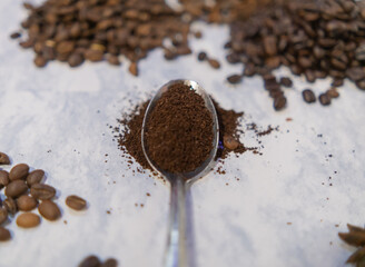 Spoonful of coffee surrounded by piles of coffee beans on white surface