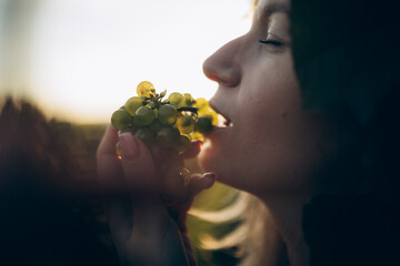 A woman is enjoying grapes in sunset light, side view.