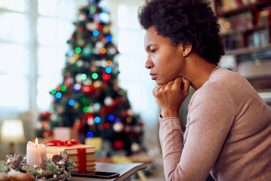 Worried African American woman thinks of something while spending Christmas alone at home.