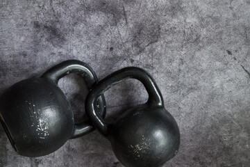 Naklejka na ściany i meble Two black kettlebells lying on their side on concrete floor, top down view, copy space.