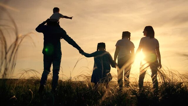 Happy family.Child and parents in field.Family walk on grass in park.Silhouette group of people in park.Child and parents walk on grass. Silhouette of family in sunshine. People walk on grass in field