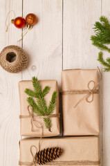 Creative DIY hobby. Making a modern handmade Christmas gift on a white wooden background. Boxes of brown craft paper, jute twine, cone, fir branches, Christmas balls, present decorations. Top view