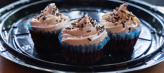Three delicious cupcakes on round black plastic tray