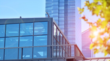 Inspiring view of the modern city. The wall of the building of glass and metal against trees. Corporate construction and ecology, view of  modern  building with blue sky and green tree. Sunlight