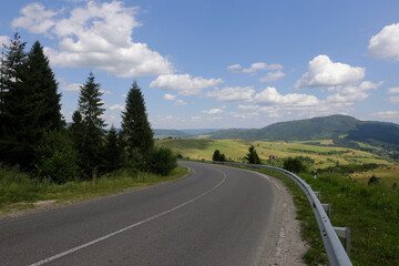 Asphalt road in a mountain in the woods, on the background of a blue sky with white clouds, Ukraine, Carpathians