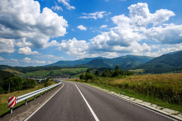 Asphalt road in a mountain in the woods, on the background of a blue sky with white clouds, Ukraine, Carpathians